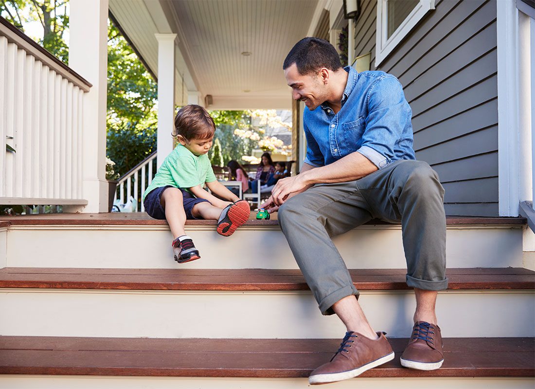 About Our Agency - View of a Happy Father Playing with his Younger Son as They Both Sit on the Steps on the Front Porch of Their Home